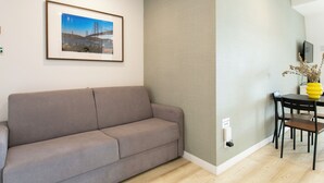 Un soggiorno con un divano, un quadro appeso al muro, un tavolo da pranzo con sedie e un vaso con fiori.