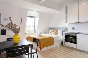 Ein modernes Hotelzimmer mit Bett, Esstisch mit Stühlen, Küchenzeile und Fenster mit Blick.