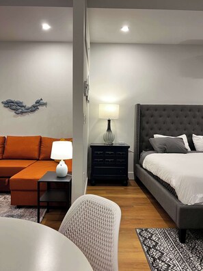 Een moderne slaapkamer met een groot bed, een bank, een klein tafeltje met een lamp en een kunstwerk aan de muur.