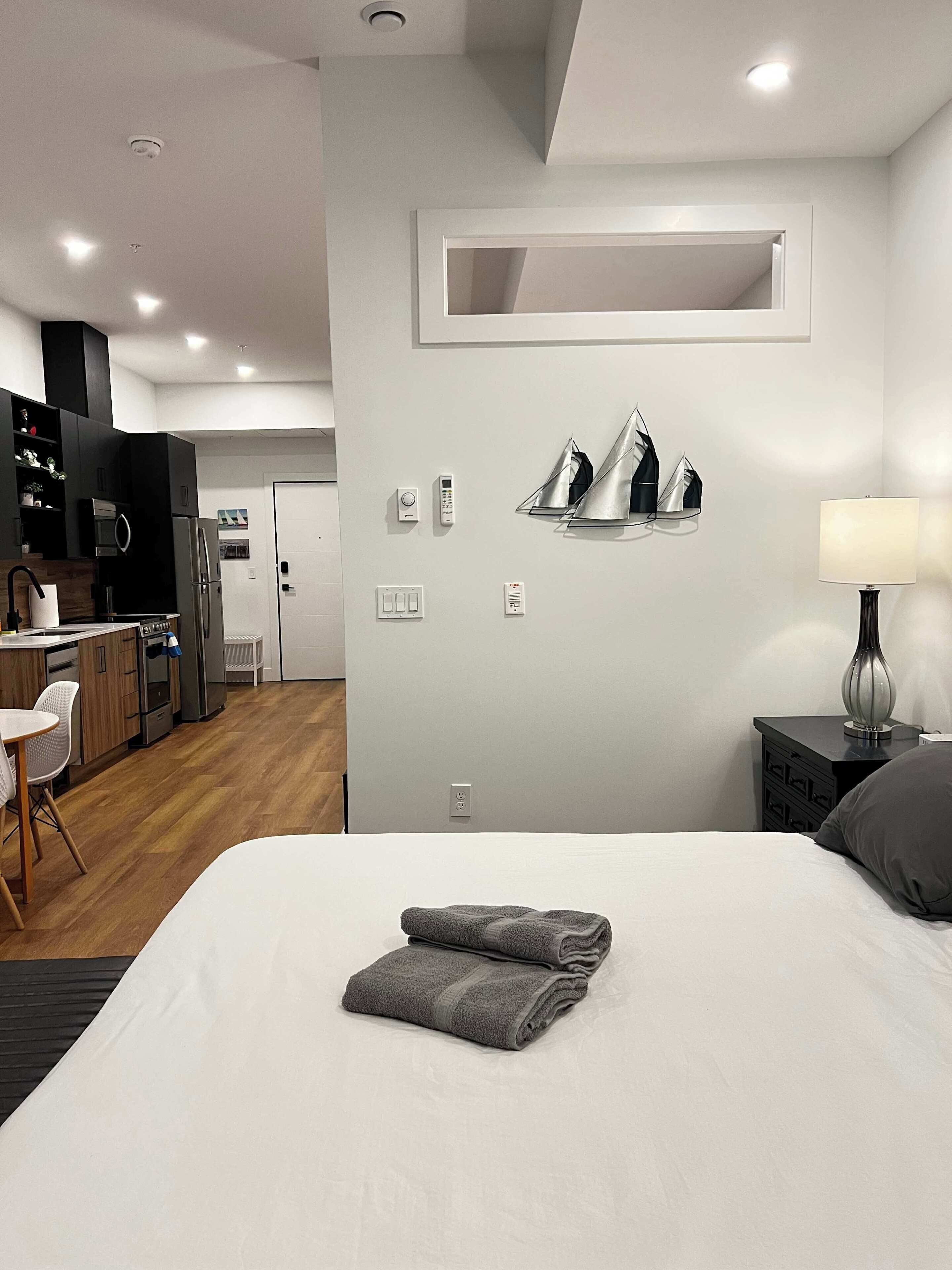 A modern hotel room with a bed, a desk, a kitchenette, and a bathroom.