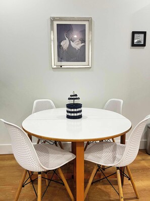 Een ronde eettafel met vier witte stoelen, een lijstwerk aan de muur erboven en een klein decoratief object op de tafel.