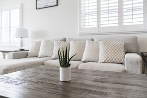 A living room with a wooden coffee table, a potted plant, a sofa with patterned cushions, and a lamp on a side table. - Bay Oasis Intercoastal Pool Home w/Hot Tub (Indian Rocks Beach)