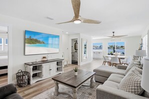 A spacious living room with a large TV, a dining area, and a view of the water. - Bay Oasis Intercoastal Pool Home w/Hot Tub (Indian Rocks Beach)