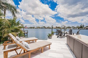 A waterfront patio with lounge chairs, a dining area, and a view of the water. - Bay Oasis Intercoastal Pool Home w/Hot Tub (Indian Rocks Beach)