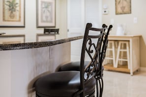 A kitchen area with a marble countertop, a black chair with a metal backrest, and a wooden cabinet in the background. - 21 Sea Club Condo Near Beach (Indian Shores)