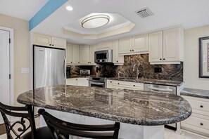 A kitchen with white cabinets, granite countertops, a stainless steel refrigerator, a microwave, and a built-in oven. - 21 Sea Club Condo Near Beach (Indian Shores)