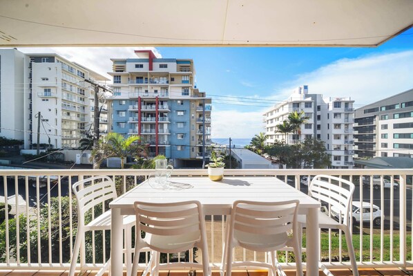 Ein Balkon mit Tisch und Stühlen mit Blick auf eine Straße mit Gebäuden und blauem Himmel.