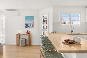 Eine moderne Küche mit einer Holzinsel, weißen Schränken und Blick auf die Stadt durch Jalousien.