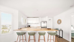 Een moderne keuken met witte kasten, een houten aanrecht en vier groene barstoelen.