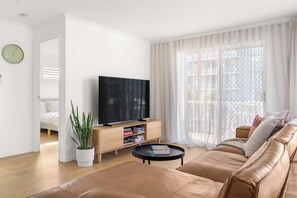 Ein modernes Wohnzimmer mit einer Ledersofa, einem Couchtisch, einem Fernseher auf einem Holzboden und einer Topfpflanze.