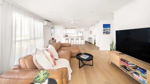 Een moderne woonkamer met een modulaire bank, een flatscreen televisie, een salontafel en een keuken op de achtergrond.