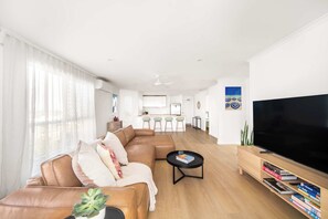 Ein modernes Wohnzimmer mit einer Eckcouch, einem Flachbildfernseher, einem Couchtisch und einer Küche im Hintergrund.