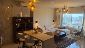 A modern living room with a sofa, dining table, chairs, and a bookshelf. - Luxury Apartment 40 m from the Beach and Bike Path (Mazatlán)