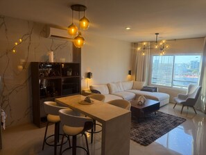 A modern living room with a sofa, dining table, chairs, and a bookshelf. - Luxury Apartment 40 m from the Beach and Bike Path (Mazatlán)