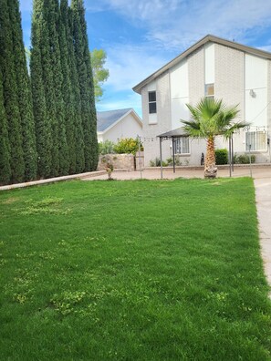 Una propiedad residencial con césped cuidado, una casa de ladrillo y árboles altos.