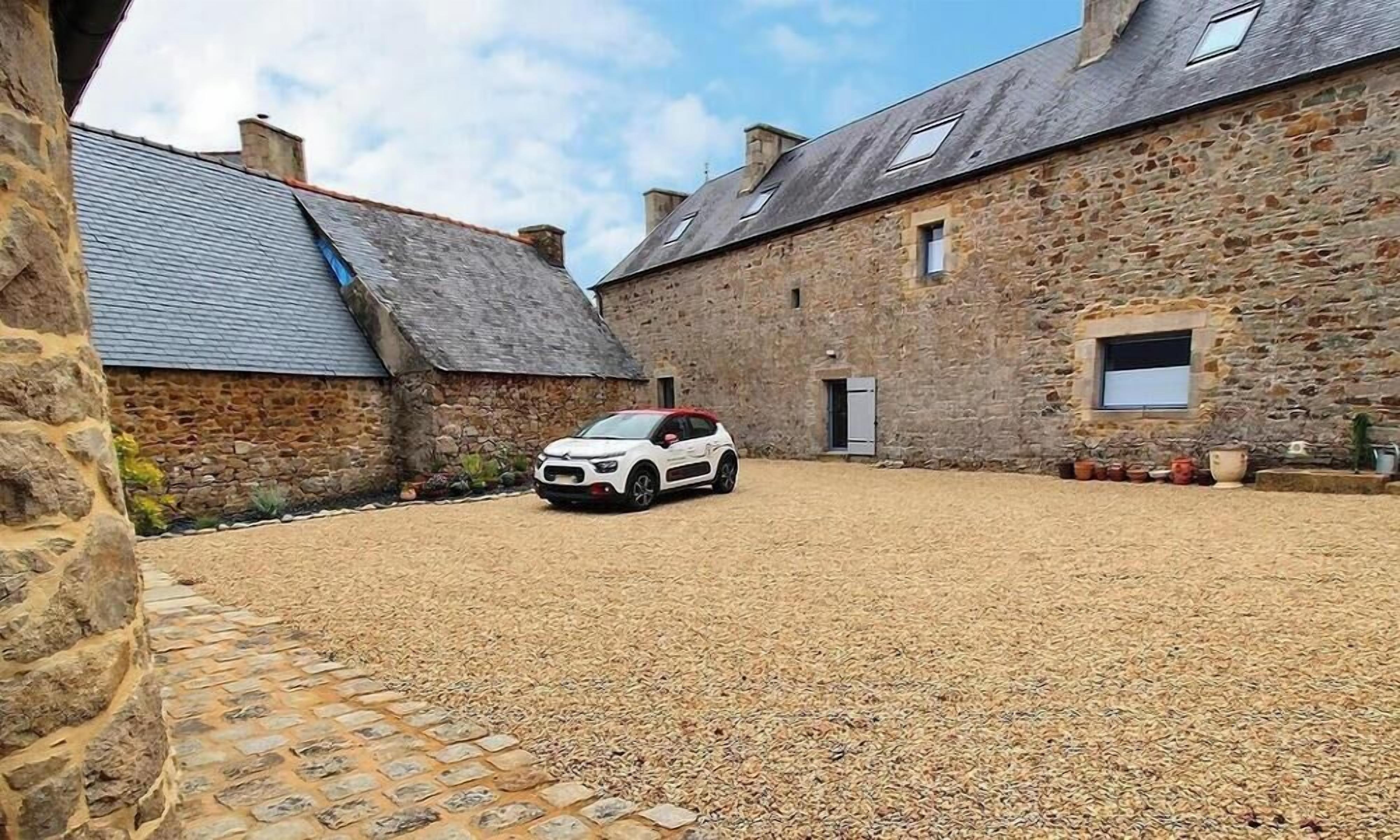 A stone building with a gravel courtyard and a parked car.