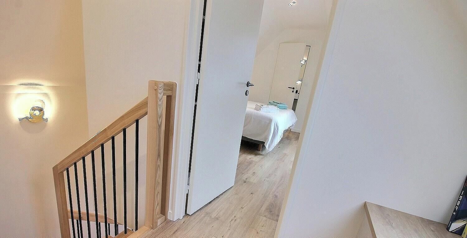 Un couloir menant à une chambre à coucher, qui contient un lit, une porte et un luminaire.
