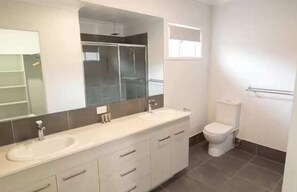 A bathroom with a double sink, a toilet, a shower enclosure, and a large mirror.