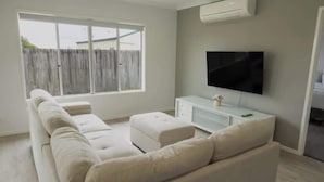 Ein Wohnzimmer mit einer Couch, einem Fernseher und einem Fenster.