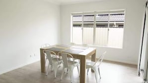 Ein Zimmer mit Holztisch, weißen Stühlen, einem Deckenventilator und einem Fenster mit Jalousien.