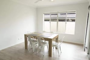 A room with a wooden table, white chairs, a ceiling fan, and a window with blinds.