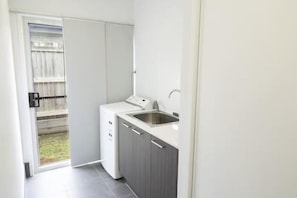 Une cuisine compacte équipée d’un lave-linge intégré, d’un évier et d’une porte coulissante donnant sur un balcon.