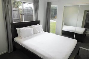 A single bed with white bedding, a dark headboard, and a window with curtains.