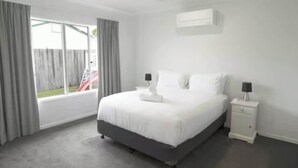 Ein Schlafzimmer mit Bett, Nachttischen, Deckenventilator und einem Fenster mit Vorhängen.