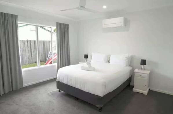 Une chambre à coucher avec un lit, des tables de chevet, un ventilateur de plafond et une fenêtre avec des rideaux.