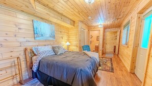 A wooden cabin interior with a bed, a lamp, and a blue chair. - Serenity Pines: Sleeps 7-Pet Friendly-Secluded forest-ATV,Snowmobile Trails close! (Newberry)