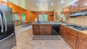 A kitchen with wooden cabinets, a refrigerator, a sink, a stove, and a dining area with a table and chairs. - Serenity Pines: Sleeps 7-Pet Friendly-Secluded forest-ATV,Snowmobile Trails close! (Newberry)