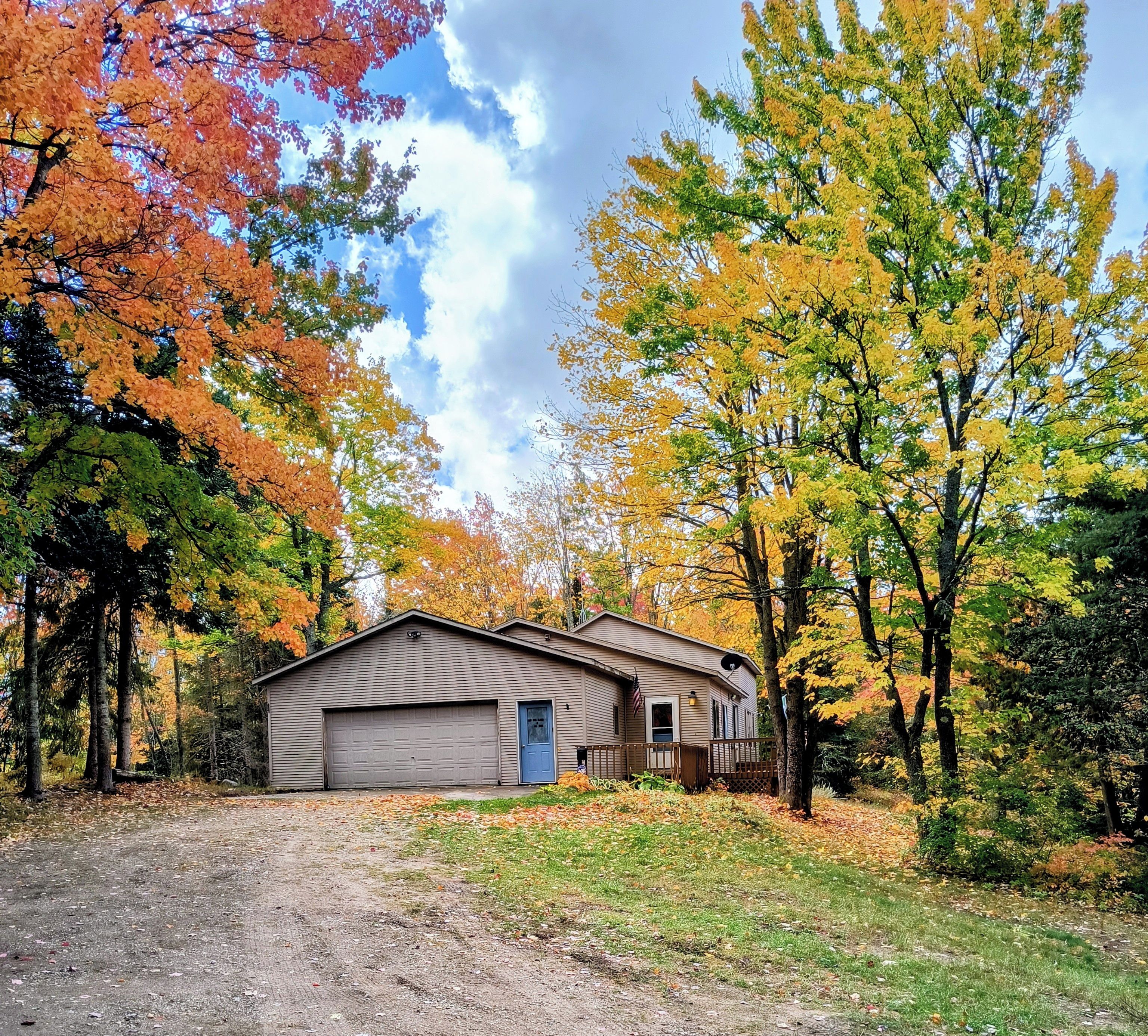 Una casetta a un piano con garage, immersa tra alberi dai colori autunnali.