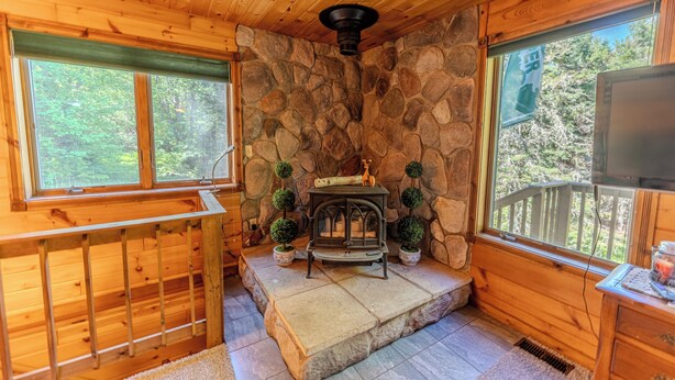 A cabin interior with a stone wall, wooden floors, a fireplace, and a television. - Serenity Pines: Sleeps 7-Pet Friendly-Secluded forest-ATV,Snowmobile Trails close! (Newberry)
