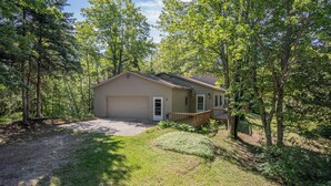 A single-story house with a front porch, surrounded by trees and a well-maintained lawn. - Serenity Pines: Sleeps 7-Pet Friendly-Secluded forest-ATV,Snowmobile Trails close! (Newberry)