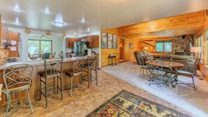 A spacious kitchen with wooden cabinets, a bar area, and a dining area with a rug. - Serenity Pines: Sleeps 7-Pet Friendly-Secluded forest-ATV,Snowmobile Trails close! (Newberry)