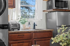 Eine Küche mit Toaster, Mikrowelle, Kühlschrank, Holzschränken, einer Granit-Arbeitsplatte und einem Fenster mit Vorhängen.