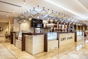 Ein modernes Café mit einer Marmor-Theke, geometrischen Pendelleuchten und einem Fernsehbildschirm.