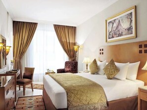 Una habitación de hotel con una cama grande, un escritorio, una silla, una lámpara y un cuadro en la pared.