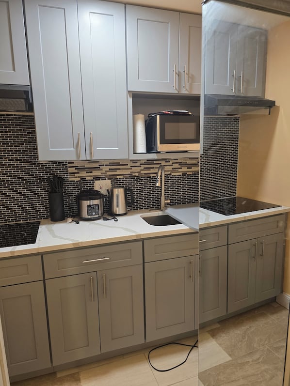 A kitchen with grey cabinets, a microwave, a kettle, and a sink.