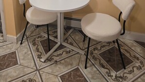Une petite table ronde avec deux chaises, une bouteille et une fenêtre avec des rideaux.