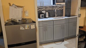Une cuisine compacte avec des meubles gris, un réfrigérateur en acier inoxydable, un four à micro-ondes et un dosseret carrelé.