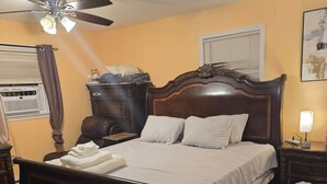 Une chambre à coucher avec un lit en bois, un ventilateur de plafond, une table de chevet, une lampe et une fenêtre avec des stores.