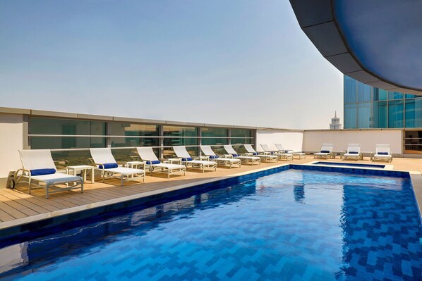 Ein Pool auf dem Dach mit Liegestühlen und einem modernen Gebäude im Hintergrund.