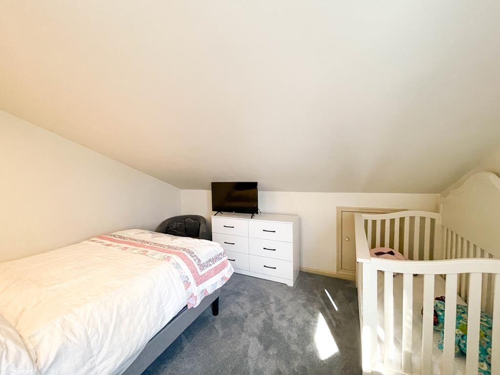 Une chambre à coucher avec un lit, une commode, un téléviseur et un berceau.
