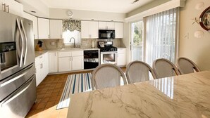 Een moderne keuken met witte kasten, roestvrijstalen apparatuur en een eethoek met een marmeren tafel en rieten stoelen.