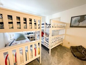 Ein Zimmer mit Etagenbetten, einer Tür, einem gerahmten Bild an der Wand und einem Teppichboden.