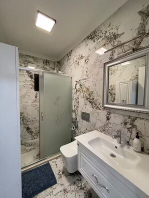 Un baño con ducha, inodoro, lavabo y paredes con diseño de mármol.