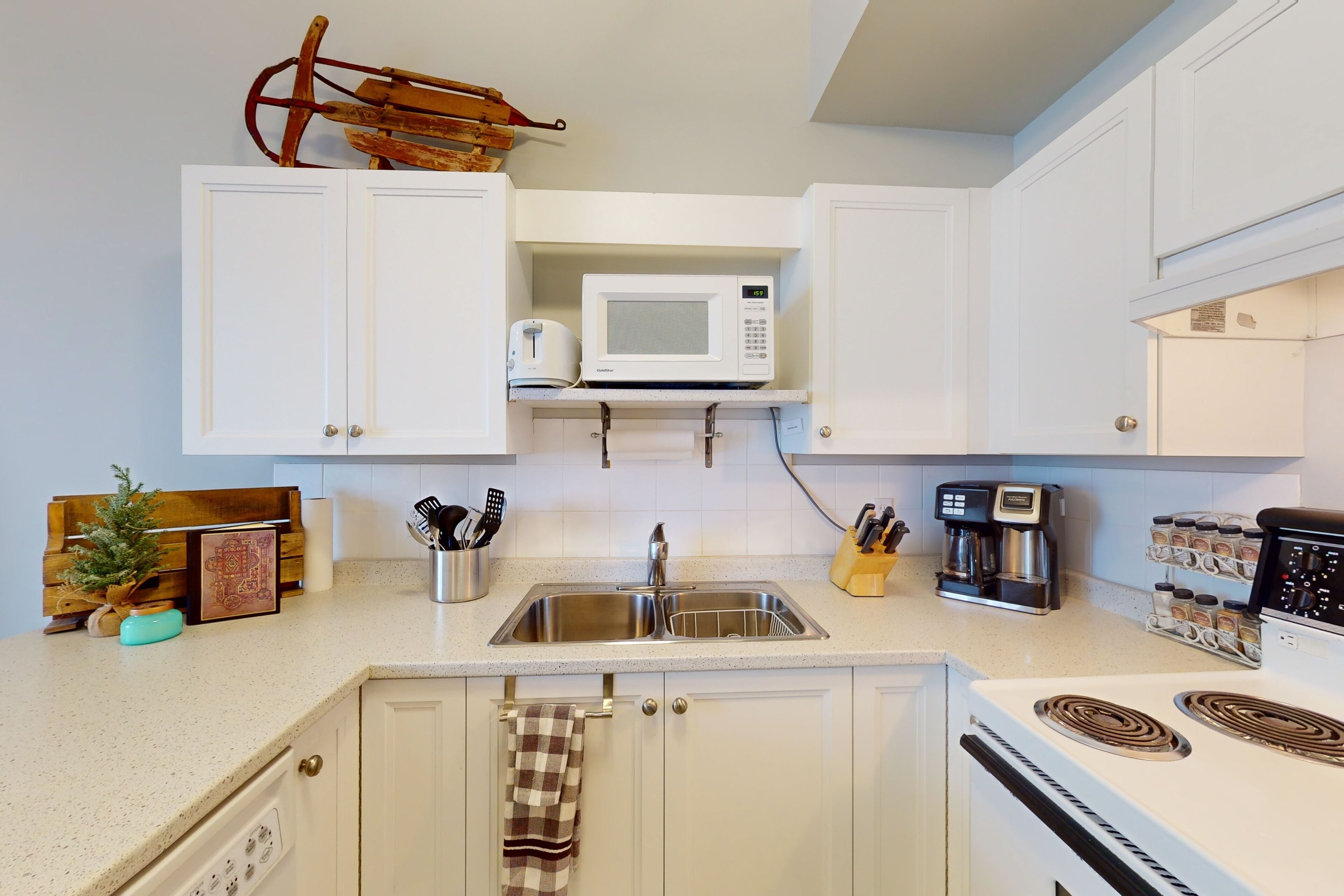 A kitchen with white cabinets, a microwave, a stove, a sink, and various kitchen utensils.