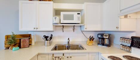 A kitchen with white cabinets, a microwave, a stove, a sink, and various kitchen utensils.