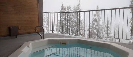 Un jacuzzi en un balcón con vista a árboles cubiertos de nieve.